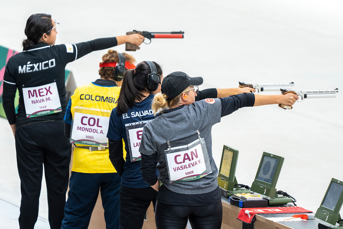 four female athletes compete in the pistol shooting competition with guns raised.